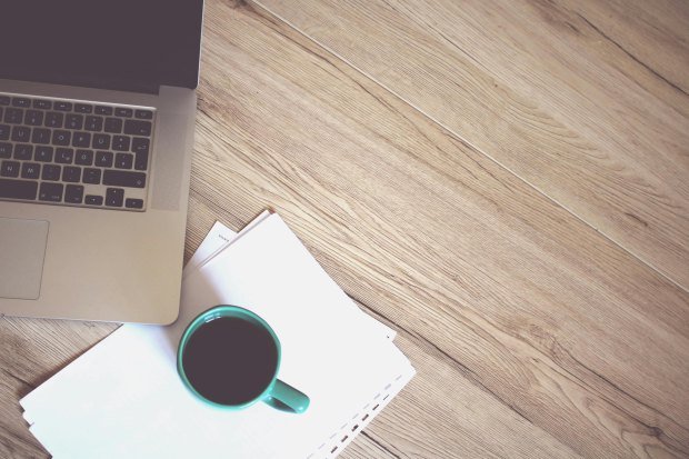 A minimalist workspace featuring a coffee cup, laptop, and wooden desk, offering a productive and stylish environment.